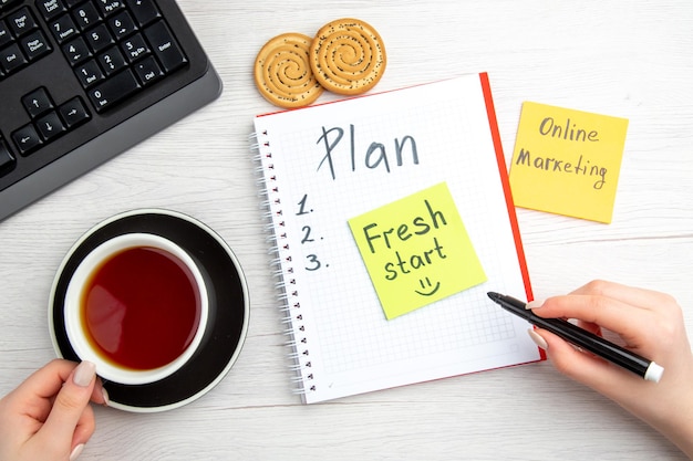 Top view cup of tea with plan schedule written notepad on white background day plan sweet school regime copybook keyboard