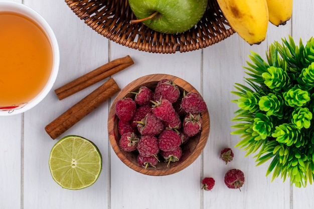 Top view of cup of tea with raspberries cinnamon and lime on a white surface