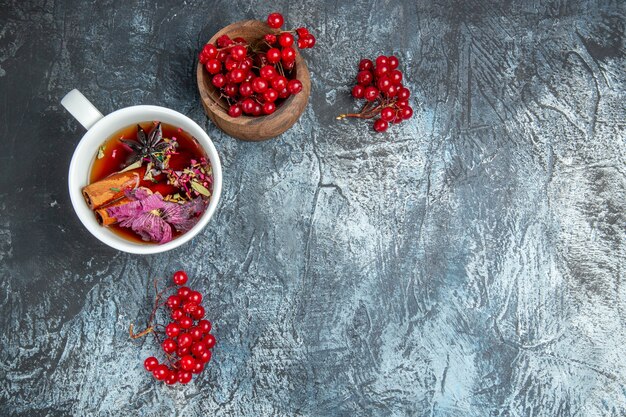 Top view of cup of tea with red cranberries on dark surface