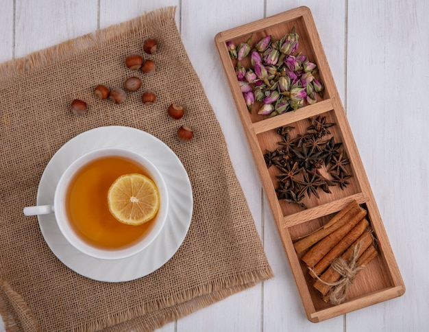 Top view cup of tea with a slice of lemon cinnamon cloves and dried rose buds on a gray background