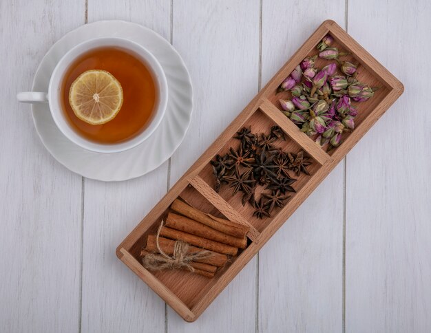 Top view cup of tea with a slice of lemon cinnamon cloves and dried rose buds on a gray background