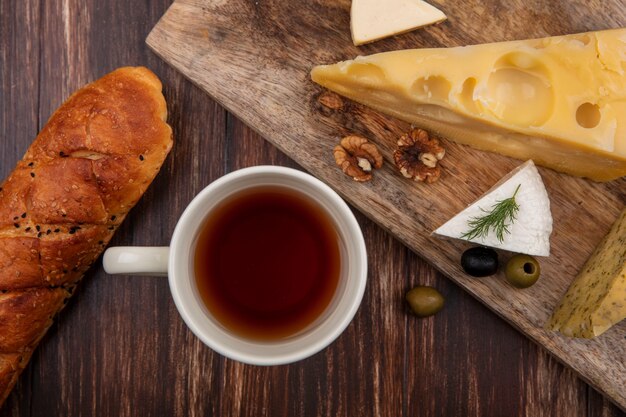 Top view cup of tea with a slice of maasdam cheese and feta cheese with olives on a board  on a wooden background