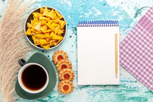 Top view cup of tea with sugar cookies and chips on light-blue surface