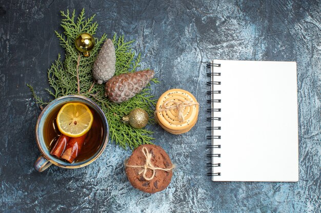 Top view cup of tea with sweet biscuits and notepad on light-dark background