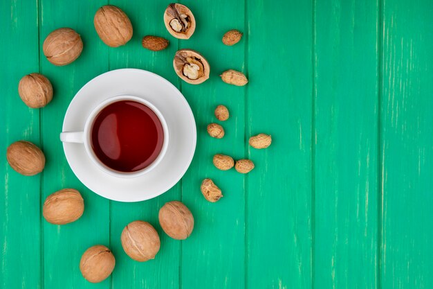 Top view of cup of tea with walnuts and peanuts on a green surface