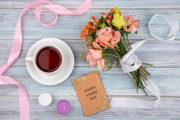 Top view of a cup of tea with wonderful colored bouquet of flowers tied with white ribbon on grey wood