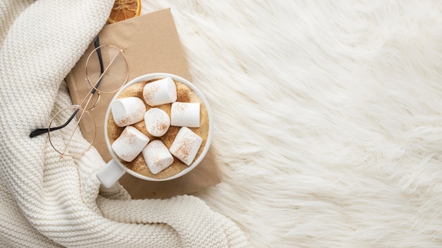 Free photo top view of cup with hot marshmallows and glasses on book