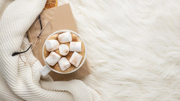 Top view of cup with hot marshmallows and glasses on book