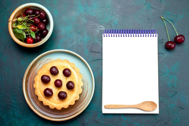Top view of cupcake with cherries next to cherries and notebook