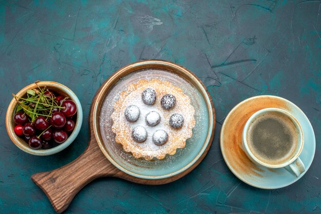 Top view of cupcake with round cherries and sugar powder next to cherries plate and latte