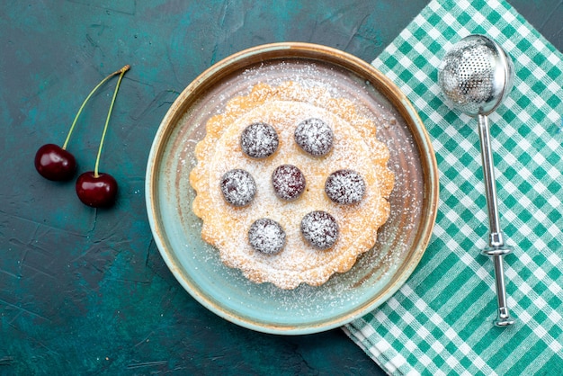 Top view of cupcake with sugar powder next to bunch of cherries