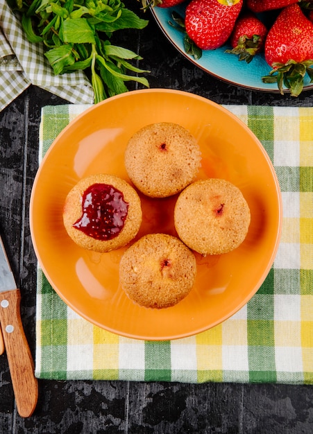 Foto gratuita cupcakes vista dall'alto con marmellata di fragole min e fragola fresca su sfondo nero