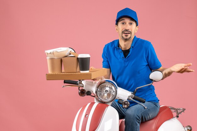 Top view of curious courier man wearing hat sitting on scooter on pastel peach background