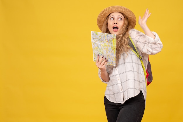 Вид сверху любопытной путешествующей девушки в шляпе и рюкзаке с картой на желтом