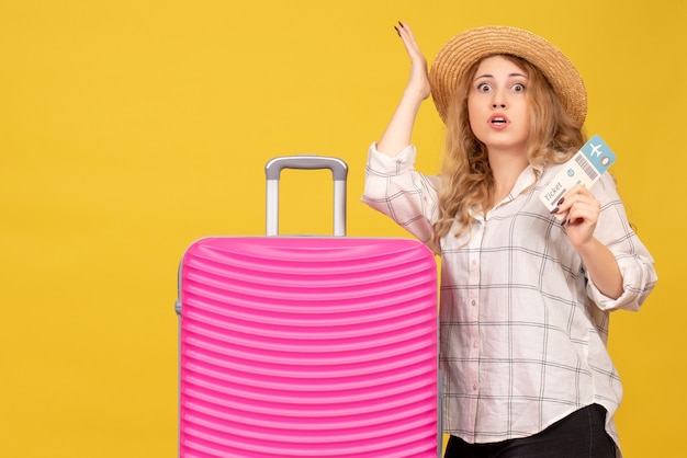 Top view of curious young lady wearing hat showing ticket and standing near her pink bag