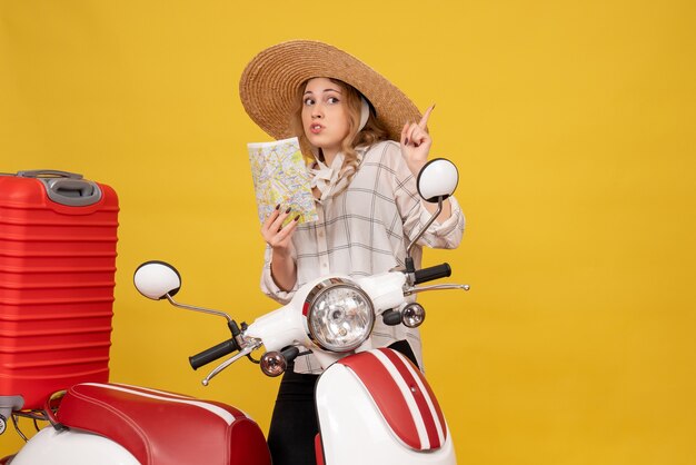 오토바이에 앉아지도를 가리키는 그녀의 짐을 수집하는 모자를 쓰고 호기심이 젊은 여자의 상위 뷰