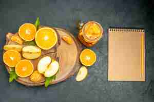 Free photo top view cut apples and oranges on wood board cocktail a notebook on dark background