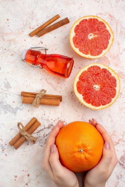 Top view cut grapefruits cinnamon sticks bottle grapefruit in female hand on nude surface
