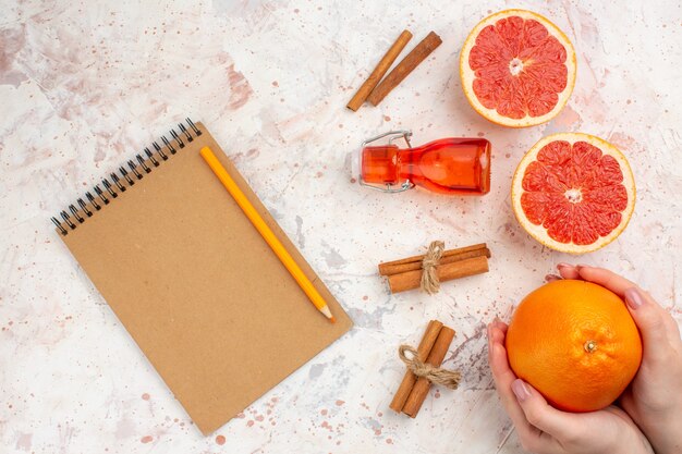 Top view cut grapefruits cinnamon sticks bottle notebook yellow pencil grapefruit in female hand on nude surface