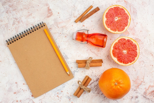 Top view cut grapefruits cinnamon sticks bottle notebook yellow pencil on nude surface