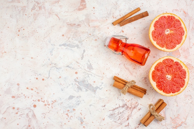 Top view cut grapefruits cinnamon sticks bottle on nude surface with copy space