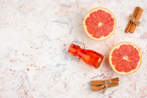 Top view cut grapefruits cinnamon sticks bottle on nude surface with copy space