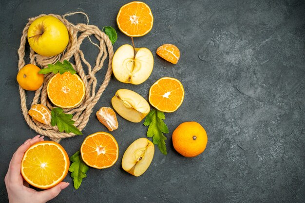 Top view cut oranges and apples cut orange in female hand on dark background