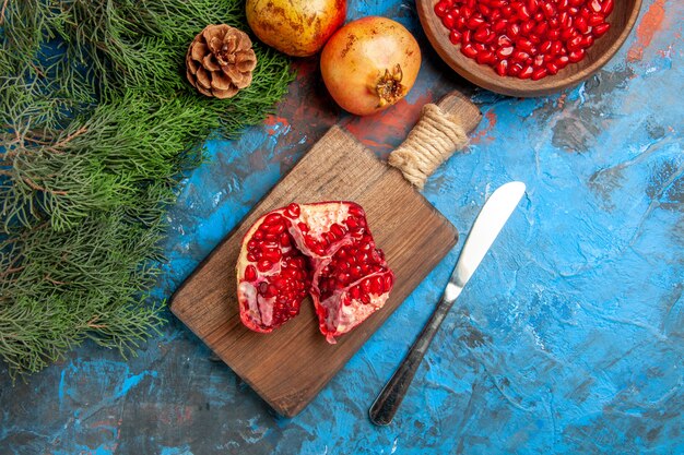 Top view a cut pomegranate on chopping board dinner knife a bowl of pomegranate seeds on blue background