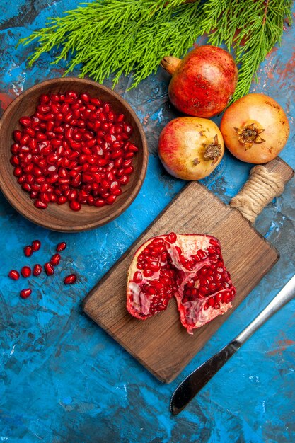 Top view a cut pomegranate and dinner knife on chopping board pomegranate seeds in bowl and pomegranates on blue background