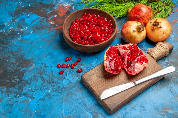 Top view a cut pomegranate and dinner knife on chopping board pomegranate seeds in bowl and pomegranates on blue background