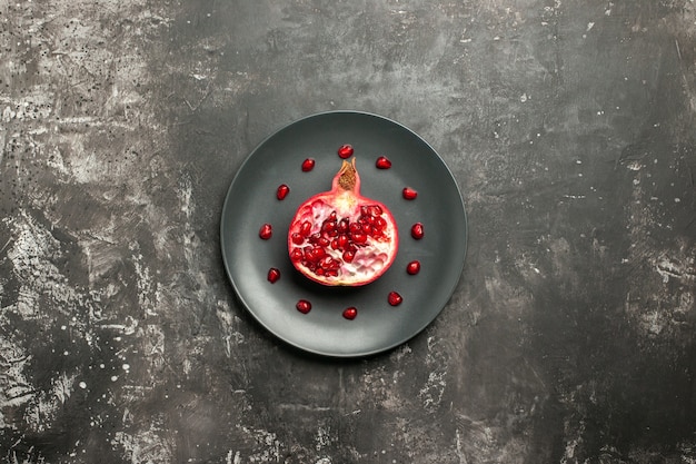 Top view cut pomegranate on oval plate on dark background