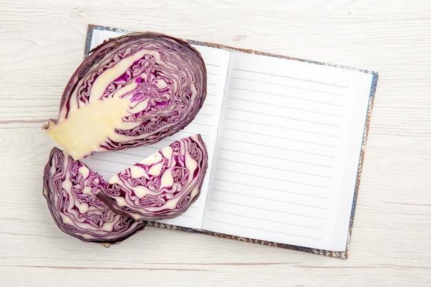 Free photo top view cut red cabbages on notebook on whte wooden table