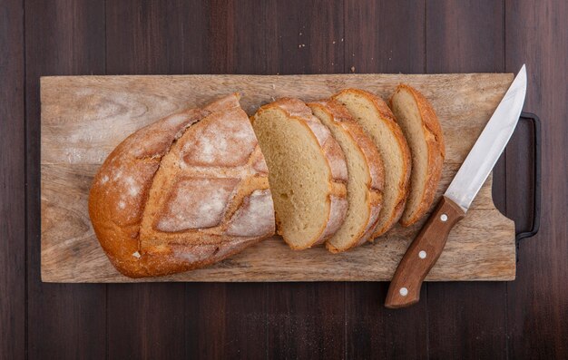 Top view of cut and sliced crusty bread with knife on cutting board on wooden background