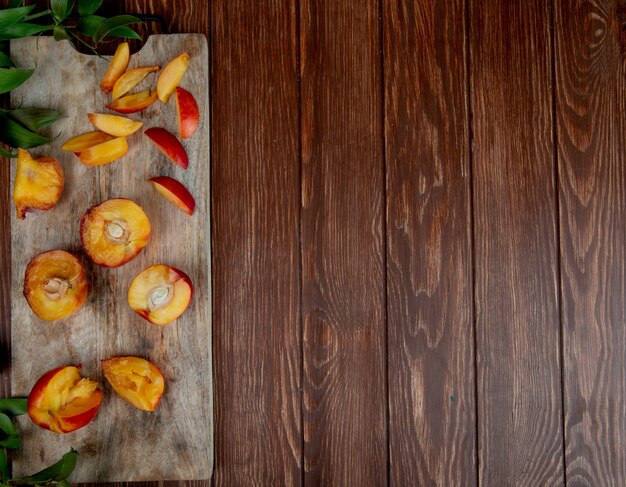 Top view of cut and sliced peaches on cutting board on left side and wooden surface with copy space