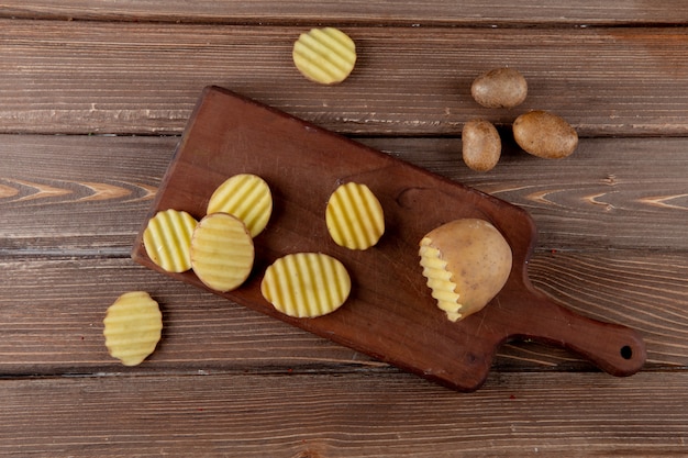 Top view of cut and sliced potato on cutting board with whole ones on wooden background with copy space