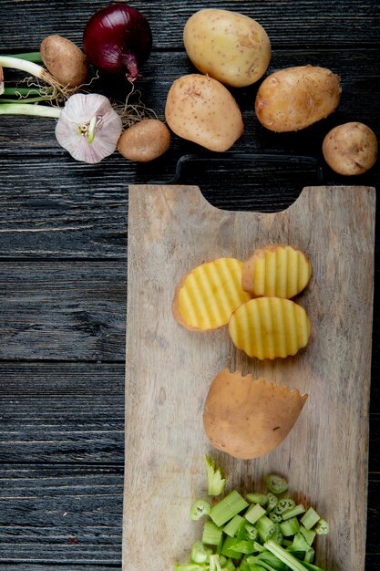 Top view of cut vegetables as potato and celery on cutting board with other vegetables on wooden background with copy space