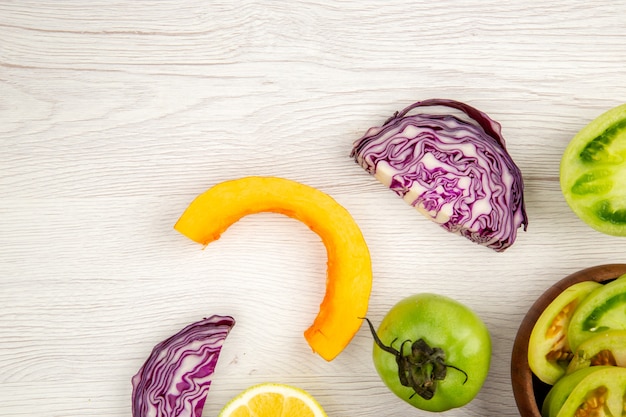 Top view cut vegetables red cabbage green tomato pumpkin red onion bell pepper caulifower lemon in wooden bowls on white wooden surface free place