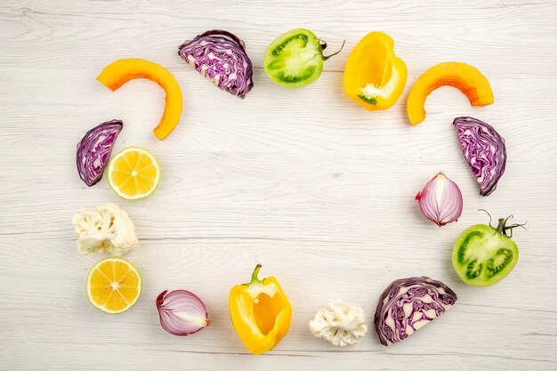 Top view cut vegetables red cabbage green tomato pumpkin red onion yellow bell pepper caulifower lemon on white wooden surface free place