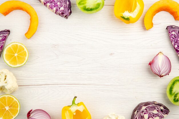 Top view cut vegetables red cabbage green tomato pumpkin red onion yellow bell pepper caulifower lemon on white wooden surface with free place