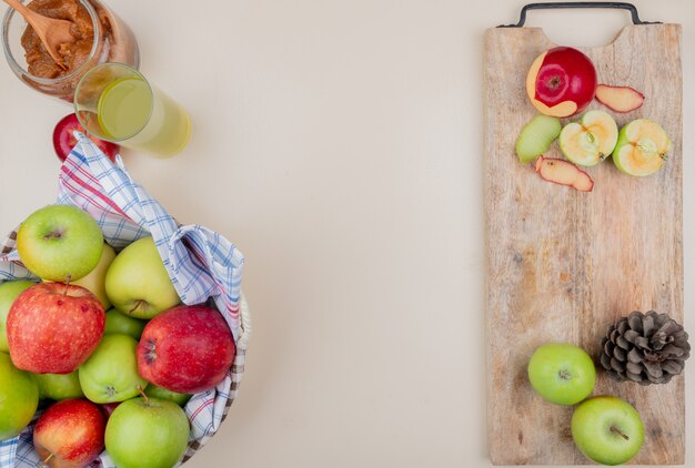 Top view of cut and whole apples with shell and pinecone on cutting board with apple jam basket of apples and apple juice on ivory background with copy space