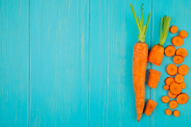 Top view of cut whole sliced carrots on right side and blue background with copy space