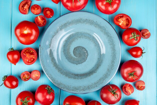 Top view of cut and whole tomatoes around plate on blue surface