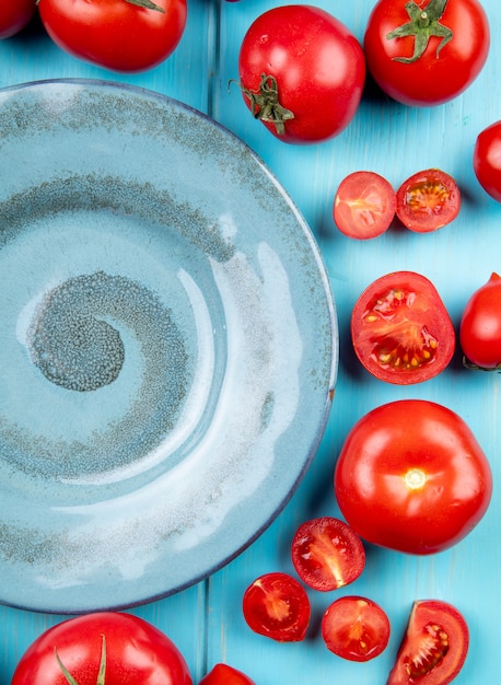 Foto gratuita vista dall'alto di pomodori tagliati e interi intorno al piatto sulla superficie blu