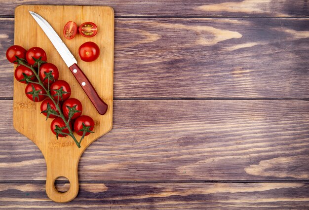 Top view of cut and whole tomatoes with knife on cutting board on wood with copy space