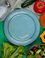 Foto gratuita vista dall'alto di verdure intere e tagliate come pomodoro basilico cetriolo lattuga con sale pepe nero e piatto vuoto sulla superficie verde
