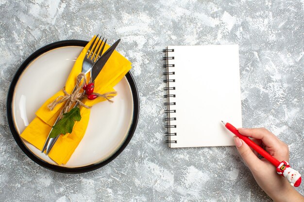 Top view of cutlery set for meal on a white plate and hand writing on closed notebook on ice surface