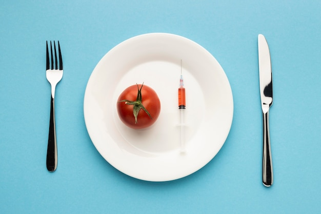 Top view cutlery and tomato with syringe