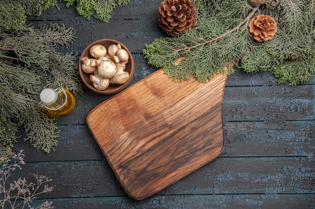 Top view cutting board cutting board under the bowl of mushrooms bottle of oil and branches