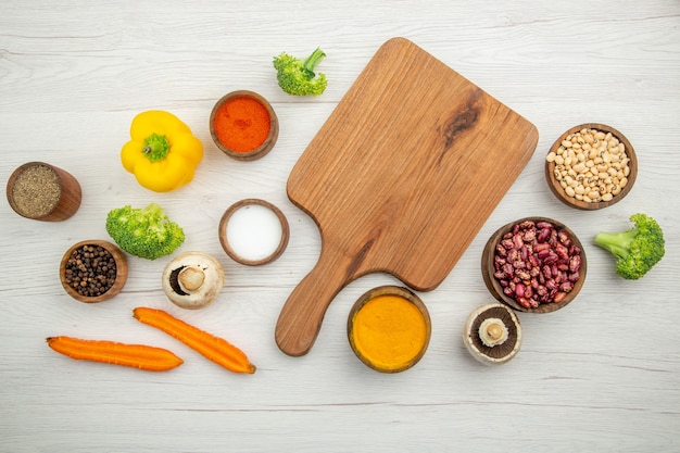 Top view cutting board mushrooms broccoli beans bowls different spices cut carrots on table