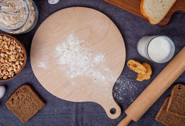 あずき色の背景に小麦粉とミルクオート麦フレークトウモロコシ麺棒でまな板の上から見る